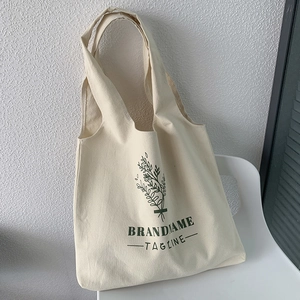 Detail of a cream canvas tote bag with green botanical prints resting on a white chair