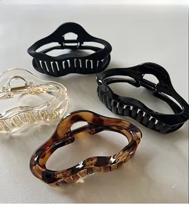 Detail view of four stylish wave-shaped hair claws in matte black, clear, and tortoiseshell