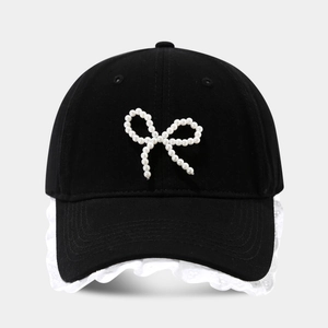 Detail of baseball cap featuring pearl bow decoration and white lace trim on the brim