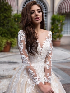 Detail of sheer long lace sleeves and intricate floral embroidery on an ivory wedding dress