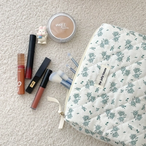Quilted floral cosmetic bag with carry handle and makeup accessories on beige carpet