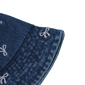 Detail of blue denim bucket hat showing white bow embroidery and high-quality stitching