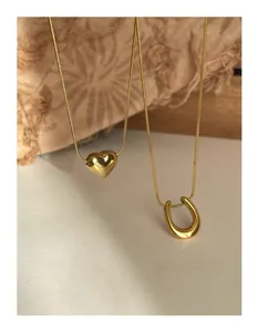 Detailed view of layered gold snake chain necklaces with heart and U-shaped pendants