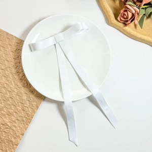 Detailed close-up of a glossy white satin ribbon bow with long streamers on a ceramic plate