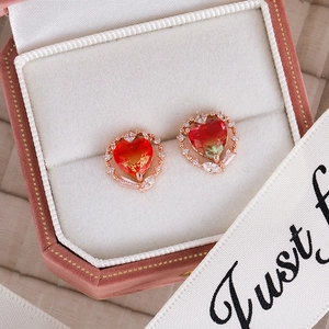 Macro detail of heart-shaped earrings with red-orange gradient zircon in a pink velvet box
