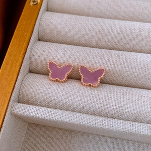 Detail of rose gold butterfly earrings with purple shell inlay on beige fabric base