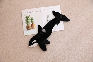 Detailed top view of a black and white orca plush stationery bag on a beige rug