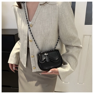 Detail of a black leather saddle bag with a metallic chain strap on a beige blazer