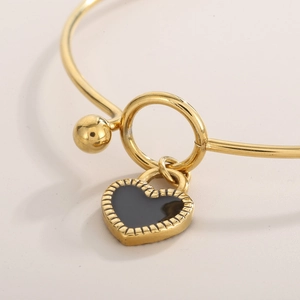 Close-up of gold heart bangle with black enamel pendant and polished metal texture