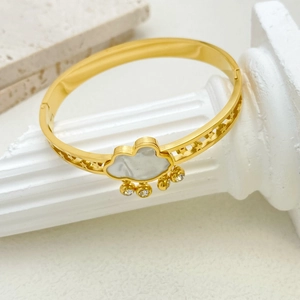 Golden clover bracelet with white cloud inlay and dangling charms on stone stand
