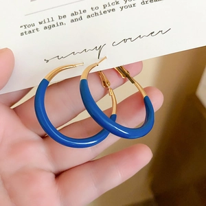 Detailed view of large gold and Klein blue circular hoop earrings with pin closure