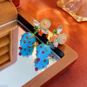 Detailed close-up of blue resin strawberry earrings with crystal embellishments on wood