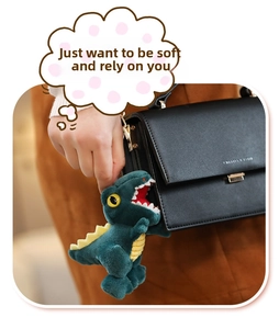 Close-up of a green plush dinosaur keychain with yellow fins hanging on a black handbag