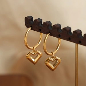 French style gold-plated titanium heart drop earrings displayed on a wooden stand