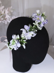 Close-up of floral crown with purple and white artificial flowers and green leaves