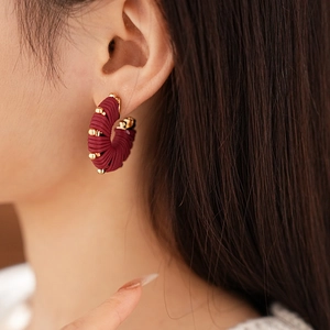 Close-up of model wearing burgundy faux leather striped U-shaped earrings with gold beads