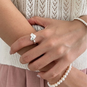 Elegant silver heart ring worn with pearl bracelets for a minimalist fashion style