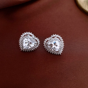 Close-up of heart-shaped zircon earrings with double halo on dark silk fabric