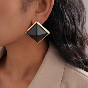 Detail view of square resin stud earrings with gold trim and black finish on a model