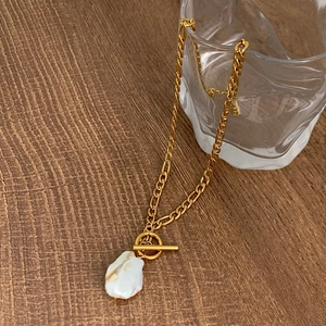 Gros plan d'un collier en perles baroques avec fermoir OT doré sur une table en bois