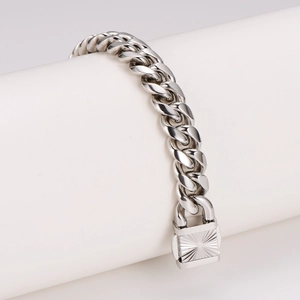 Classic silver Cuban link bracelet with engraved sunburst clasp on a white stand