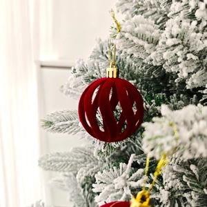 Détail d'une boule de Noël en velours rouge ajouré suspendue à une branche enneigée