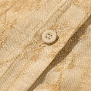 Close-up of golden jacquard fabric texture and round ivory button on the shirt set