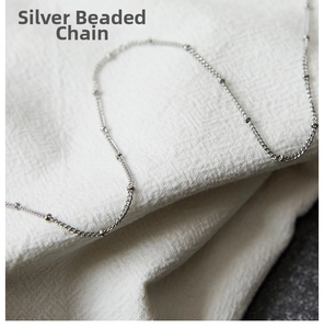 Detailed close-up of a silver beaded cable chain on a textured white linen background