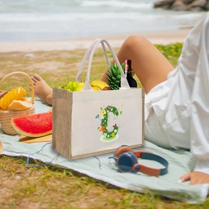 Detailed view of linen canvas tote bag with floral letter C pattern on a picnic blanket