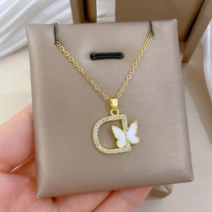 Detailed close-up of golden necklace with crystal D-letter and white butterfly pendant