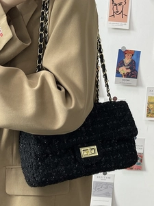 Chic black tweed crossbody bag with golden chain strap worn by a model in a casual setting