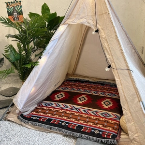 Detail of bohemian geometric rug with tassels inside a cozy beige glamping tent