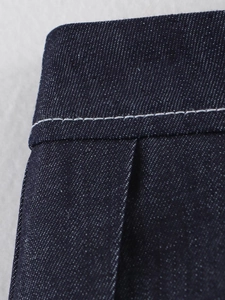 Dettaglio della gonna a pieghe in denim blu scuro con cuciture bianche a contrasto in vita