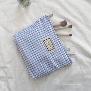 Detailed shot of blue striped toiletry bag with PLEASANT TIME label and makeup brushes