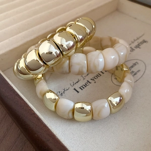 Detail of three-piece set with gold metal and cream marble resin beaded bracelets