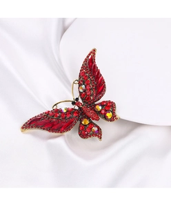Détail macro d'une broche papillon dorée avec cristaux rouges sur soie blanche