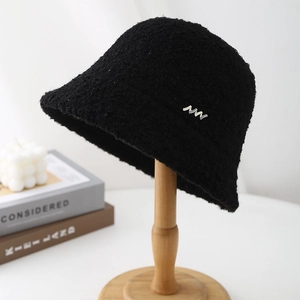 Detail of black curly plush bucket hat with a stylish silver metal logo decoration