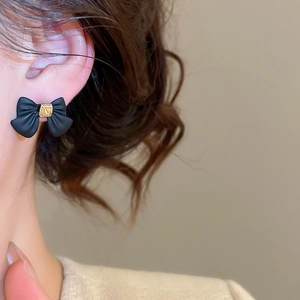 Close-up of a model wearing a matte black bow earring with golden metal center detail