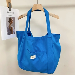 Detail view of large blue canvas tote bag with shoulder straps and front brand logo tag