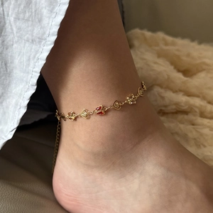 Close-up of a gold butterfly anklet with red enamel charms worn on a model ankle