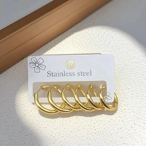 Detailed view of three pairs of polished gold stainless steel hoop earrings on a white surface