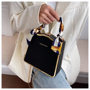 Detail of a black box bag featuring a gold metal frame and silk scarf wrapped handle
