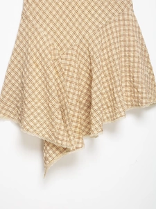 Détail de la robe plissée à carreaux beige avec texture et ourlet en dentelle blanche