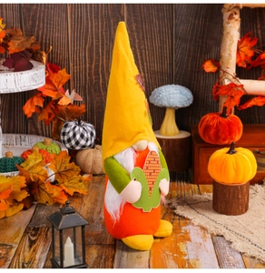 Detail of autumn gnome plush with yellow pointed hat holding corn on harvest background