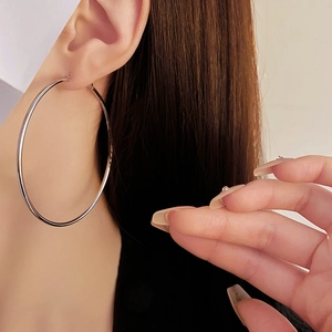 Close-up of a large silver hoop earring worn by a model to show texture and size