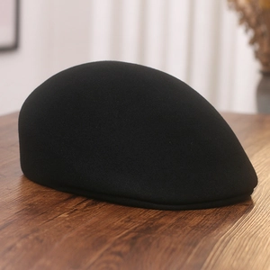 Detail of a black wool flat cap on a textured dark wood surface with soft indoor lighting