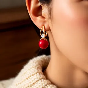 Elegant gold drop earrings with red resin bead and zircon stone worn by a model