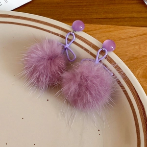 Dettaglio orecchini a fiocco viola chiaro con pompon di peluche su un piatto di ceramica