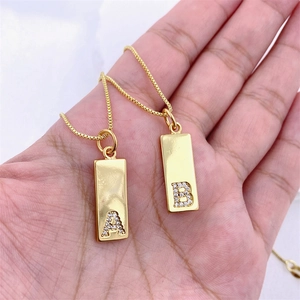 Detail of hand holding gold rectangular pendant necklaces with zircon letters A and B