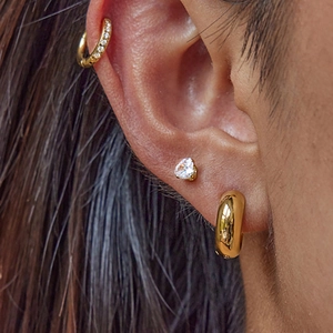 Set of three golden hoop and heart stud earrings worn elegantly on a model's ear
